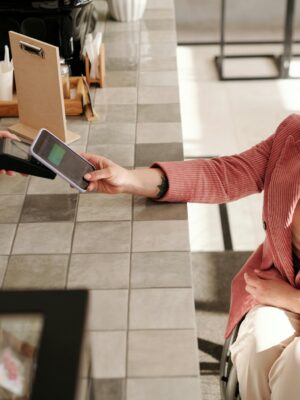 Woman in pink blazer making smartphone payment at a cafe from her wheelchair.